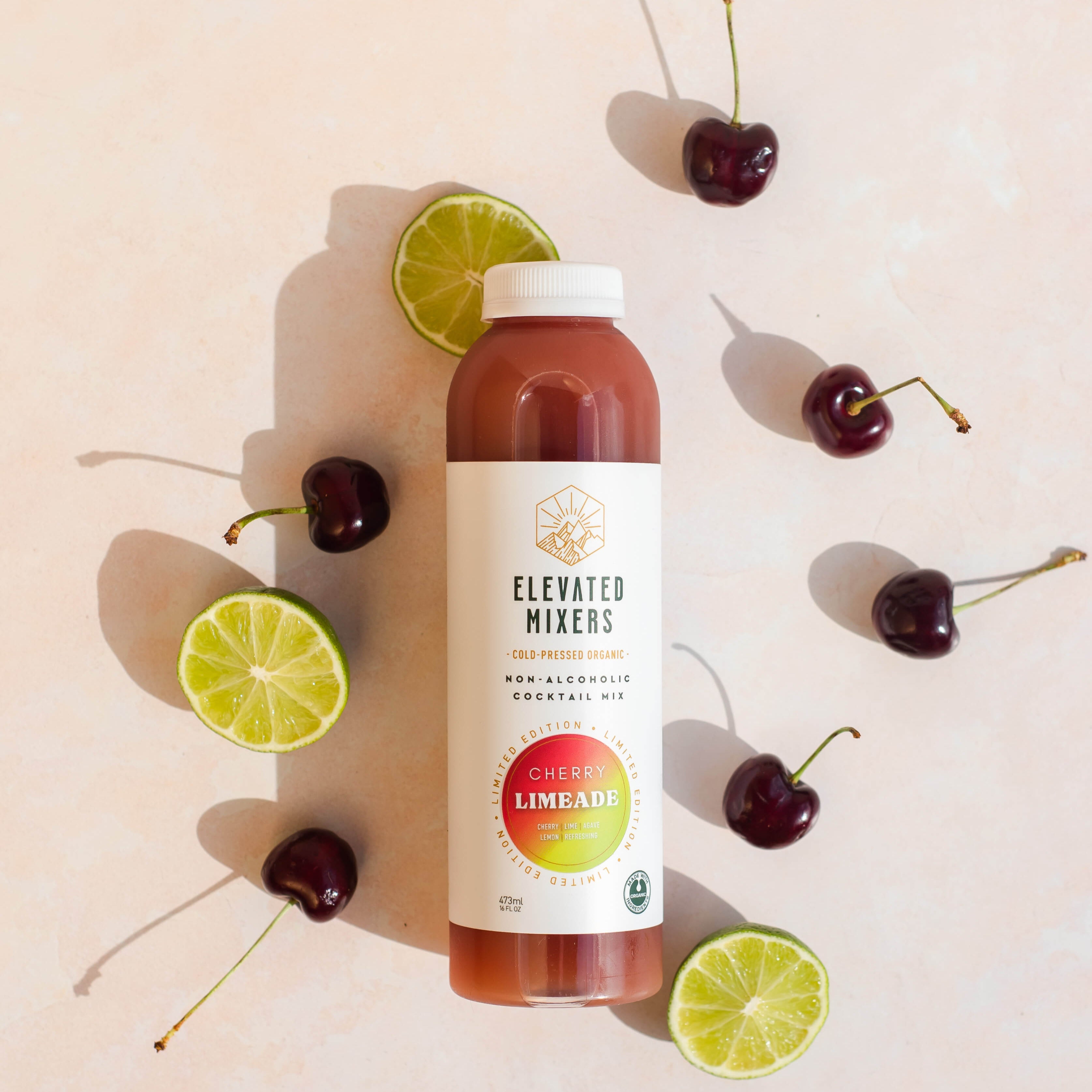Bottle of 'Elevated Mixers' limeade with cherries and lime slices on a light background