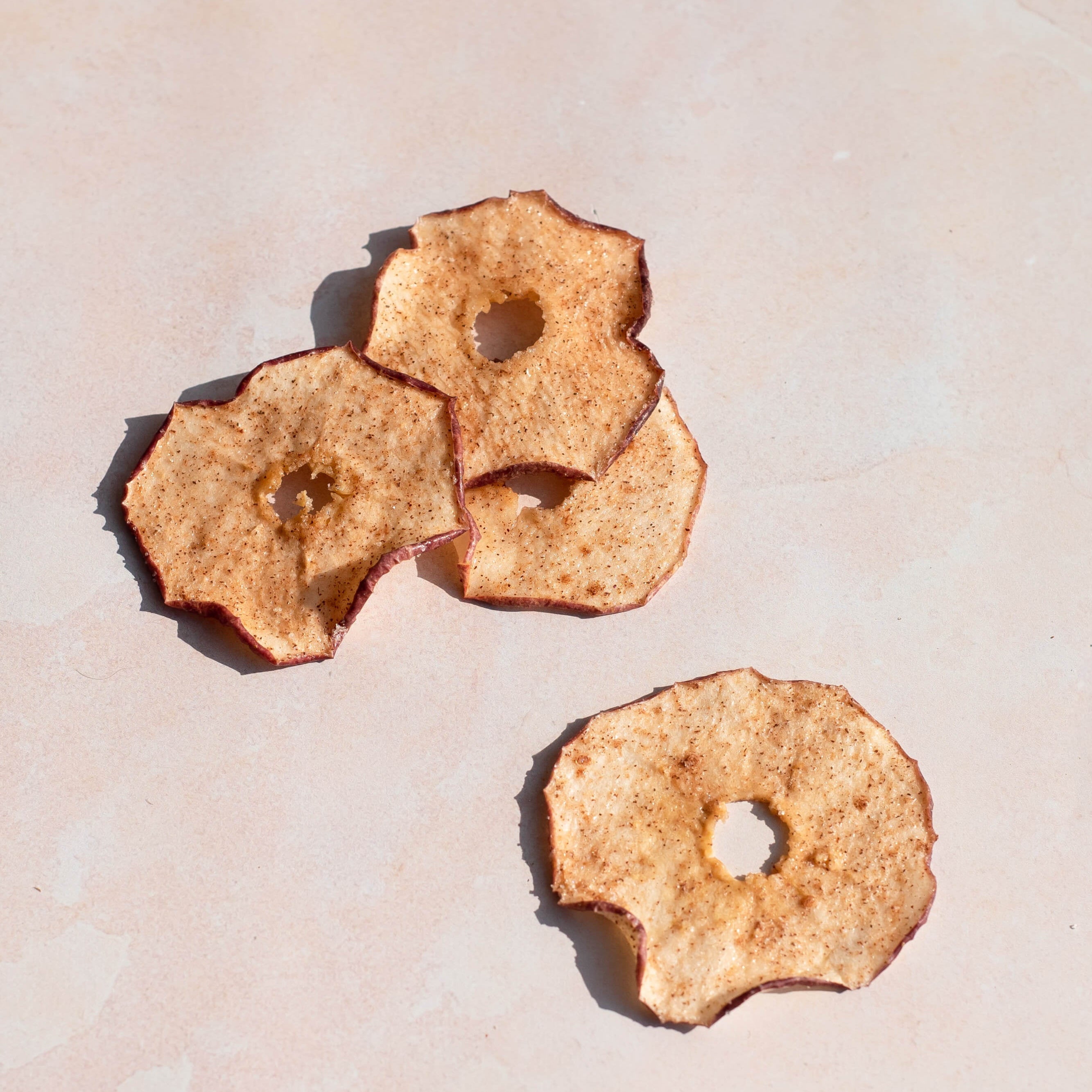 Three dried apple slices on a light beige surface